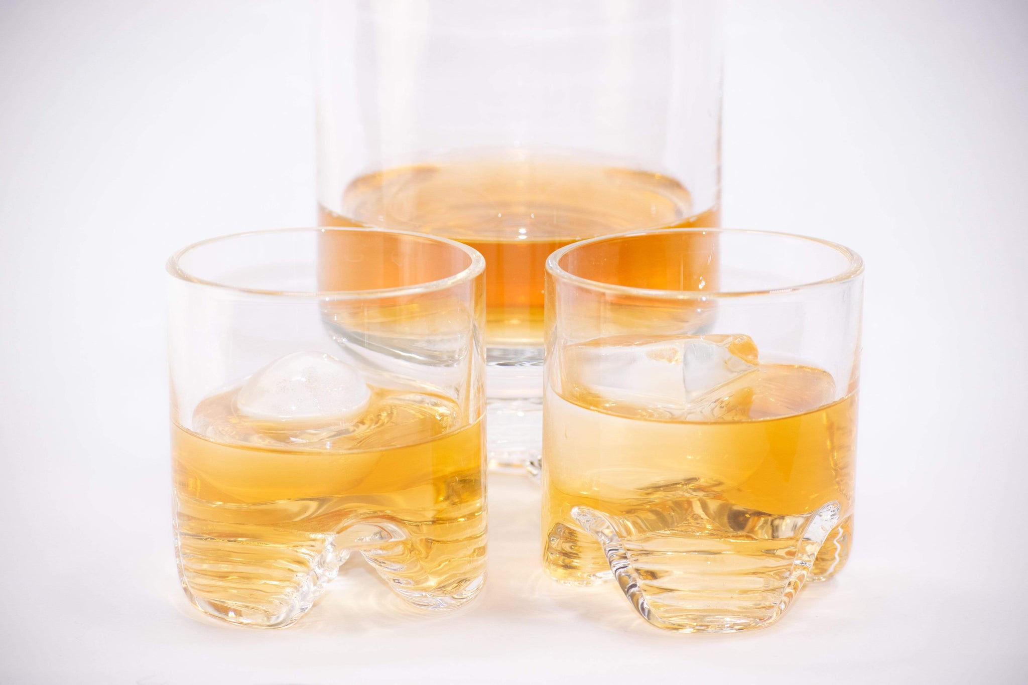 Handblown decanter holding bourbon featured with handblown glass tumblers with large clear ice cubes and spheres