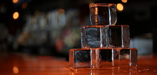 Large clear ice cubes made at home stacked up with the top cube spinning and falling to the table top