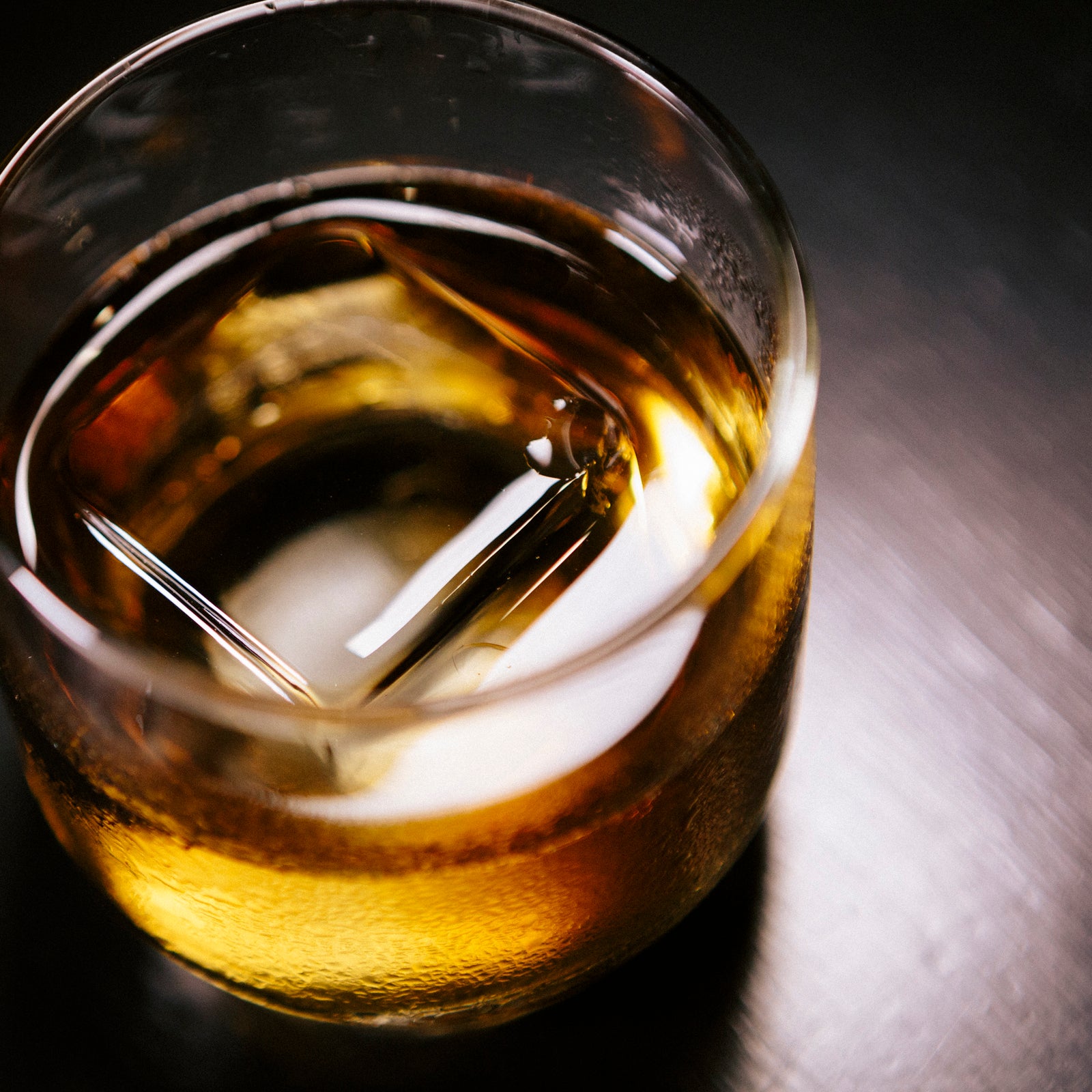 large clear ice cube floating in cocktail in a glass tumbler
